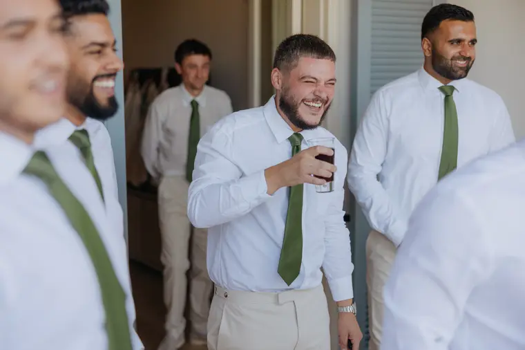 Andrew's groomsmen in green ties sharing a drink and a laugh while getting ready