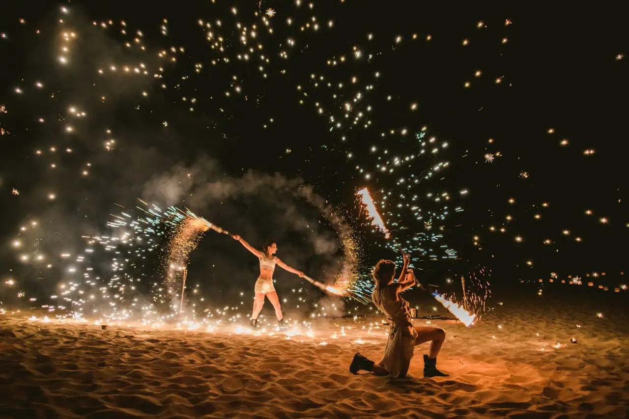 Fire performers spinning sparks on the sand at night during a destination wedding party