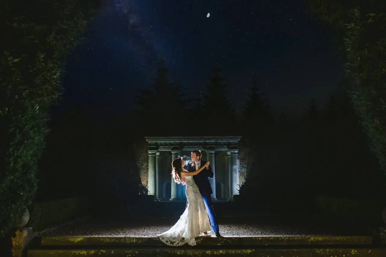 Elina and Iain embracing under a starry night sky before a lit temple folly at Wotton House, Surrey