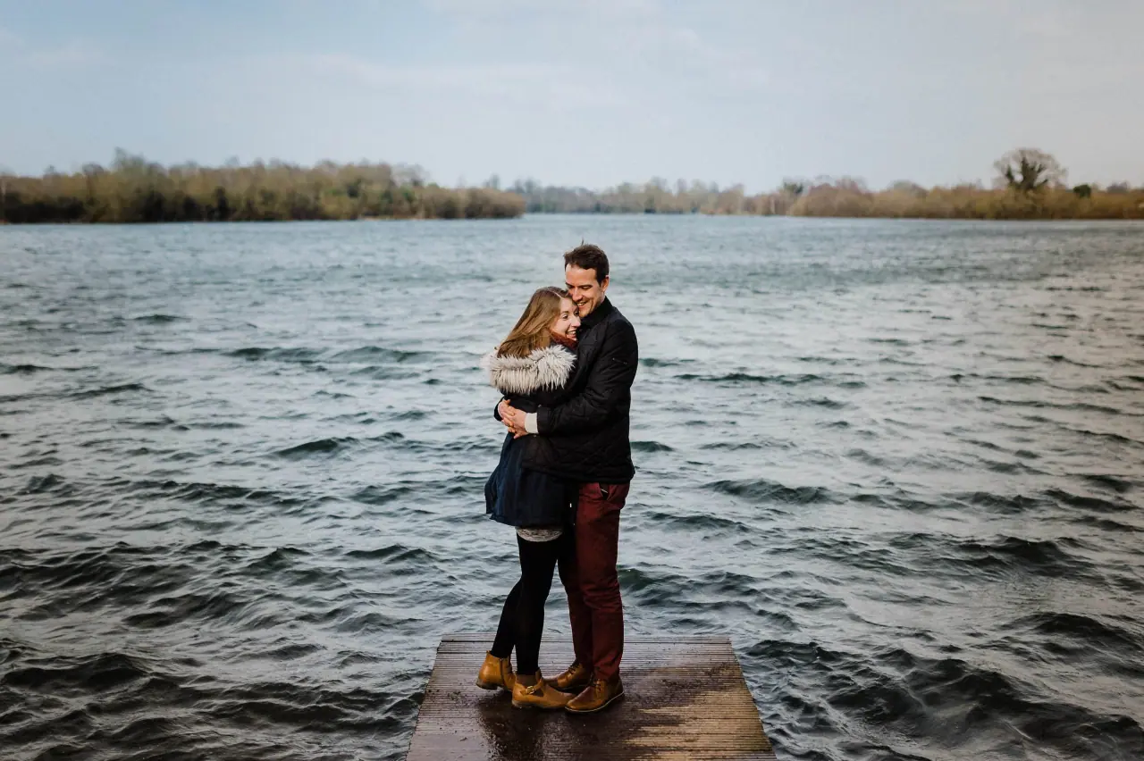 Jana and Alex embracing on a small jetty over a wind-rippled lake
