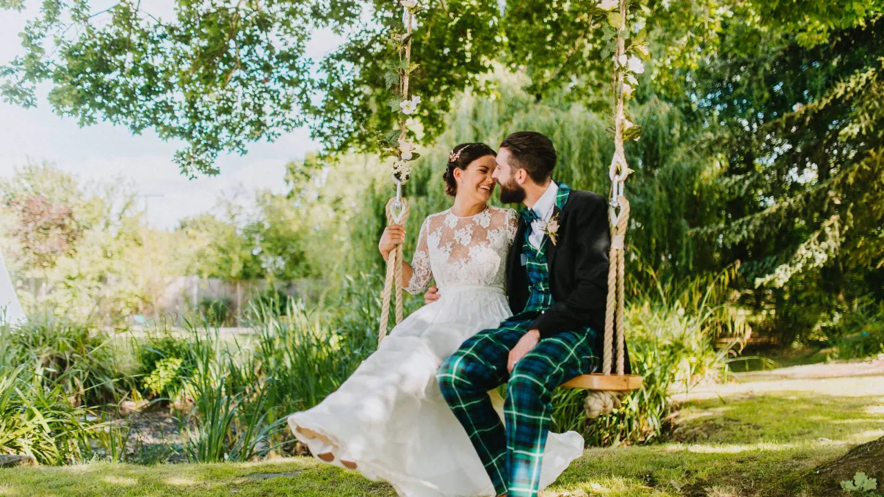 Helen and Ali sharing a rope swing in a leafy garden in Windsor, Berkshire, groom in tartan trousers