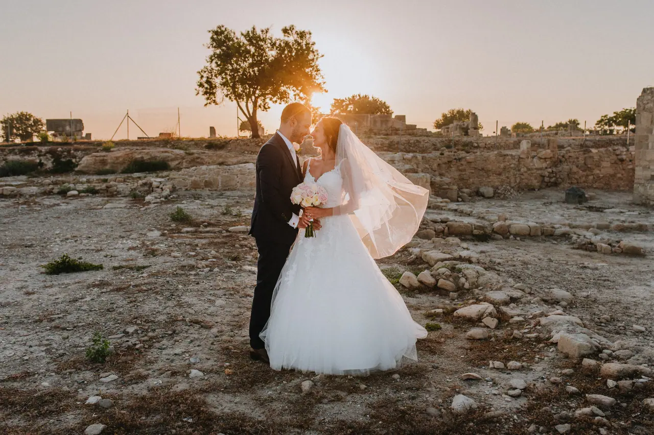 Marco and Anastassia embracing at sunset among ancient ruins near Liopetro, Kouklia, her veil lifting in the breeze