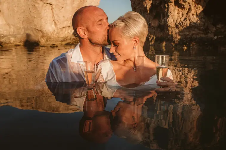 Alana and Luke toasting with champagne as they stand in a sea rock pool near Paphos