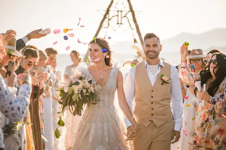 Boho bride and groom walking through a shower of confetti from cheering guests