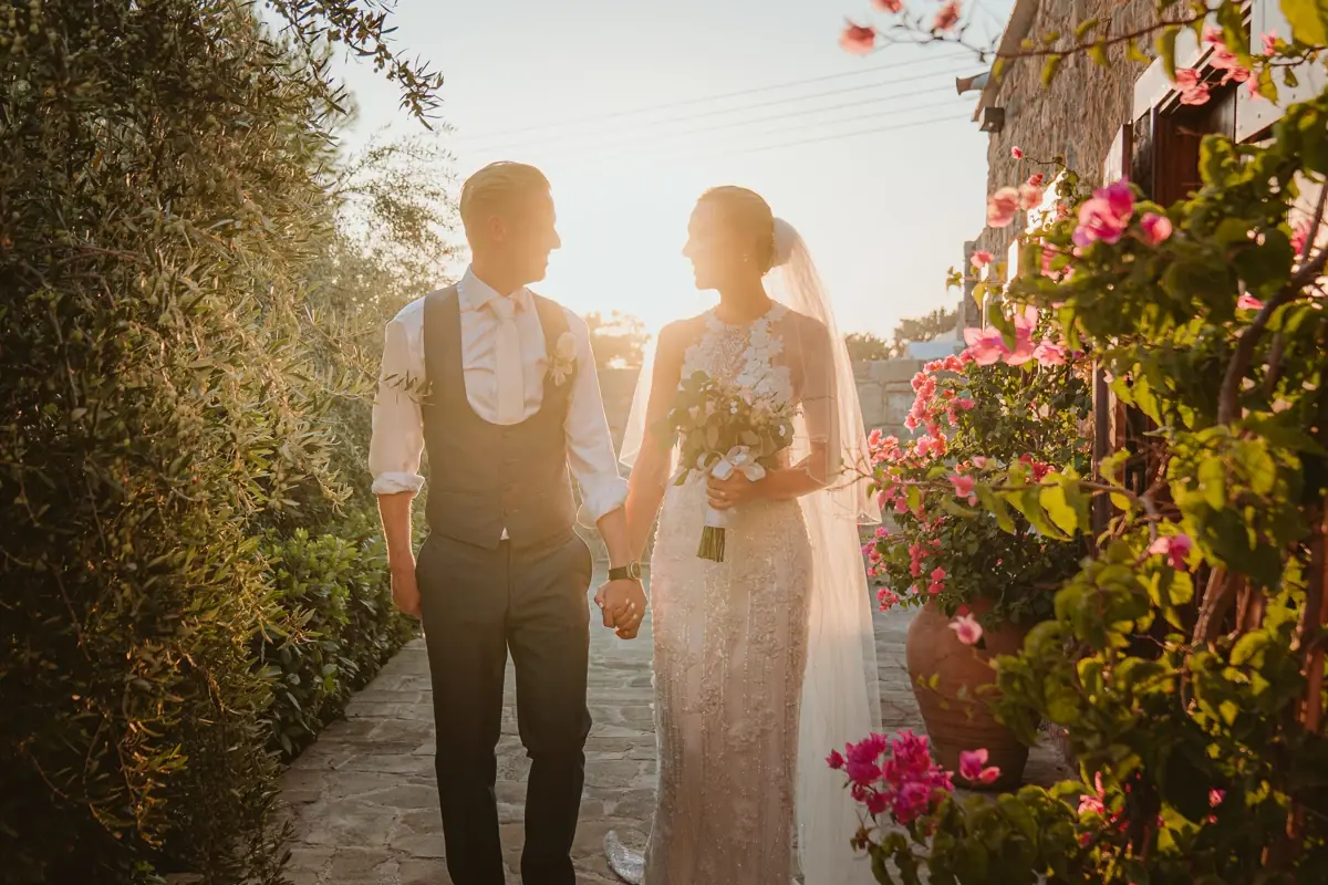 Charlene and Ben holding hands on a sunlit path lined with bougainvillea at Liopetro, Kouklia