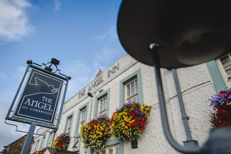 Hanging sign of The Angel of Corbridge inn with colourful flower baskets