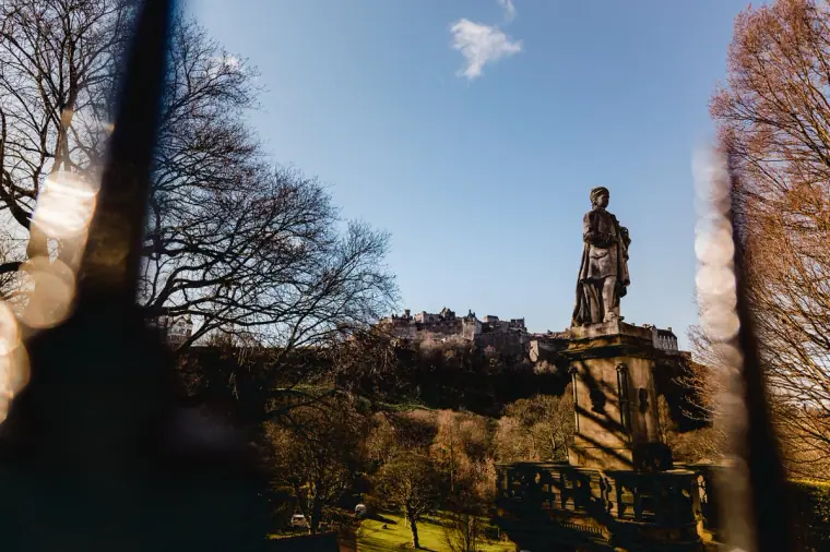 Statue silhouetted against blue sky in Princes Street Gardens, with Edinburgh Castle behind