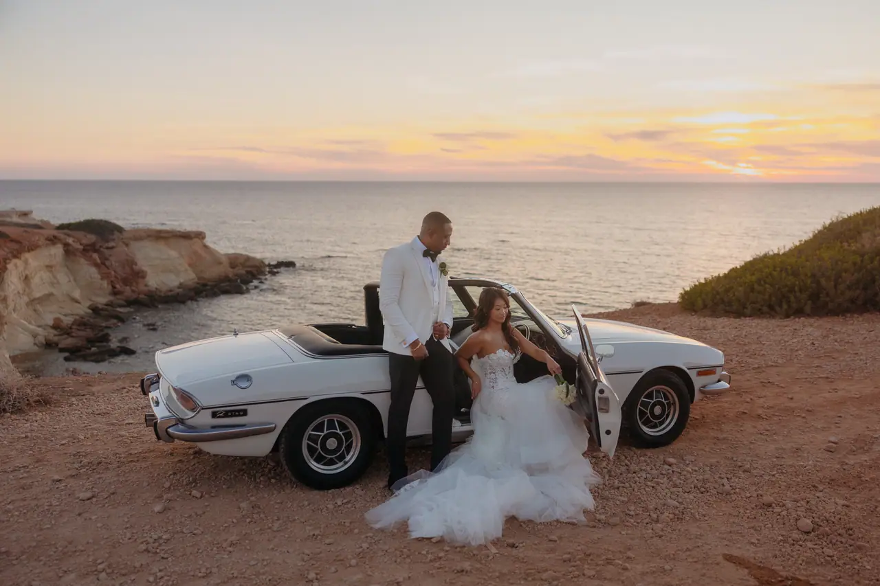 Bride and groom beside the 1977 Triumph Stag on a clifftop at sunset, Cyprus