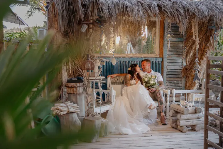Bride and groom sitting together on the deck of a rustic thatched beach bar at Sea You Beach Bar