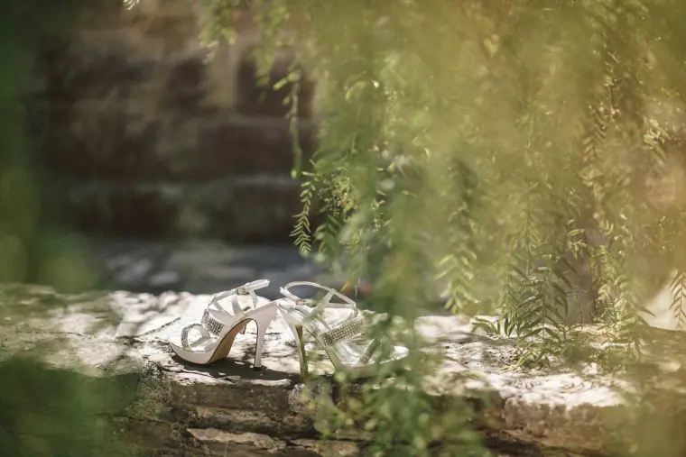 Bride's sparkly heels resting on a sunlit stone wall among greenery