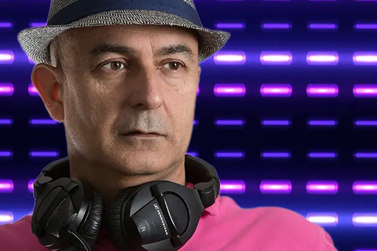Portrait of a DJ in a trilby with headphones round his neck before purple lights