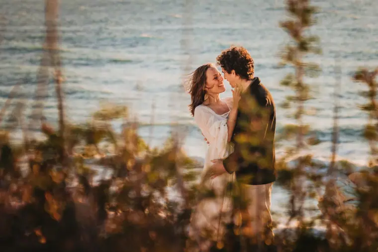 Aiko and Erez kissing on the clifftop, glimpsed through coastal shrubs