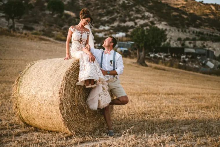 Amie sitting on a hay bale as Graeme leans beside her in a golden field