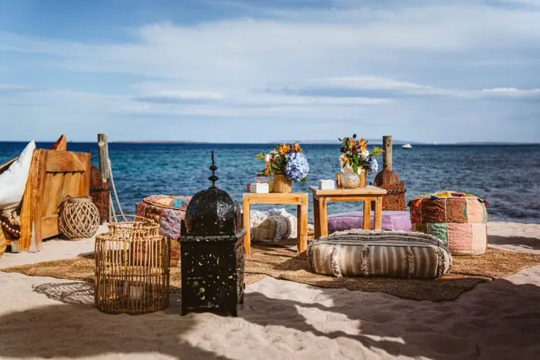 Moroccan lanterns, poufs and flower-topped tables set up on the sand by the sea at La Escollera, Ibiza
