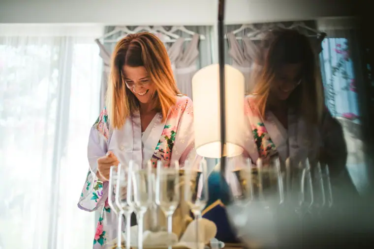 Bridesmaid in a floral robe pouring champagne into a row of glasses on the wedding morning