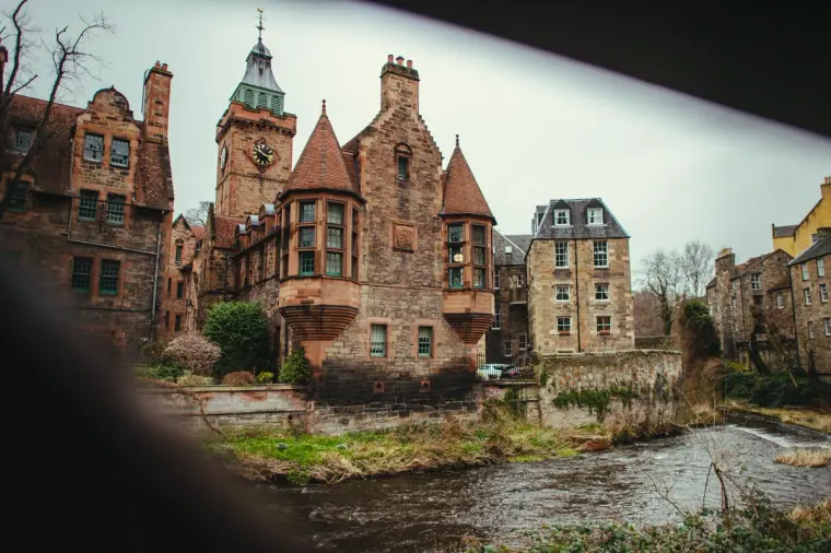 Turreted red sandstone buildings beside the river on a grey Edinburgh morning