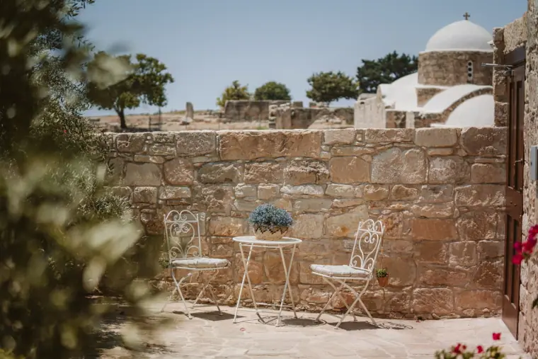 Bistro table and white iron chairs on a stone terrace beside a domed chapel at Liopetro, Kouklia