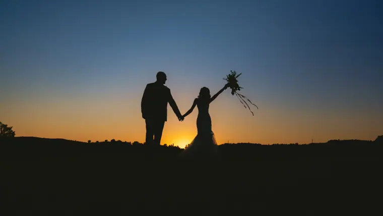 Silhouette of Emily and Chris holding hands, bouquet raised, against a twilight sky at Minthis, Paphos