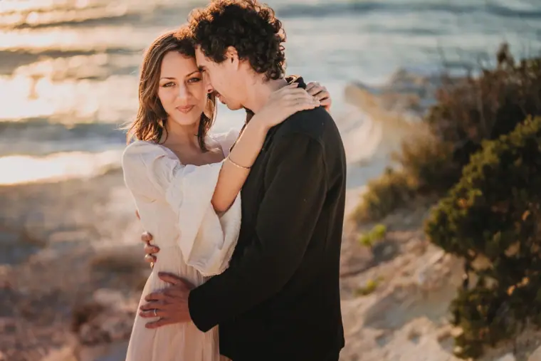 Erez holding Aiko close on the rocky coast at sunset near the Paphos sea caves