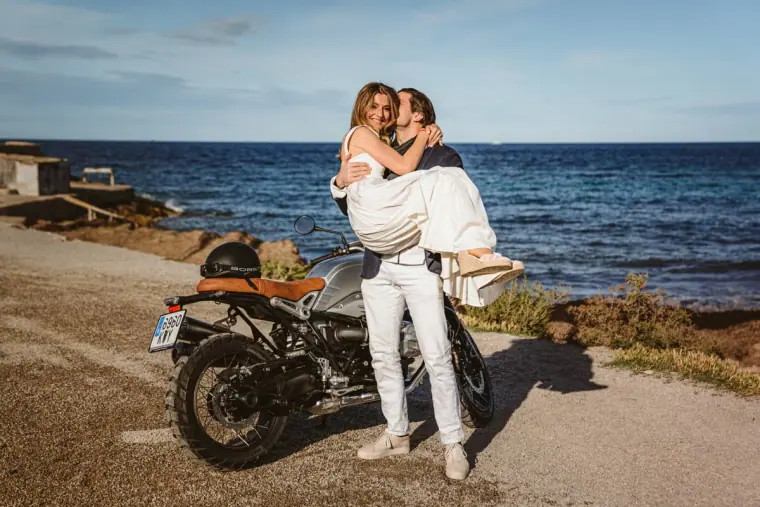 Antonia and Birger laughing as he lifts her beside a motorbike by the sea, La Escollera, Ibiza