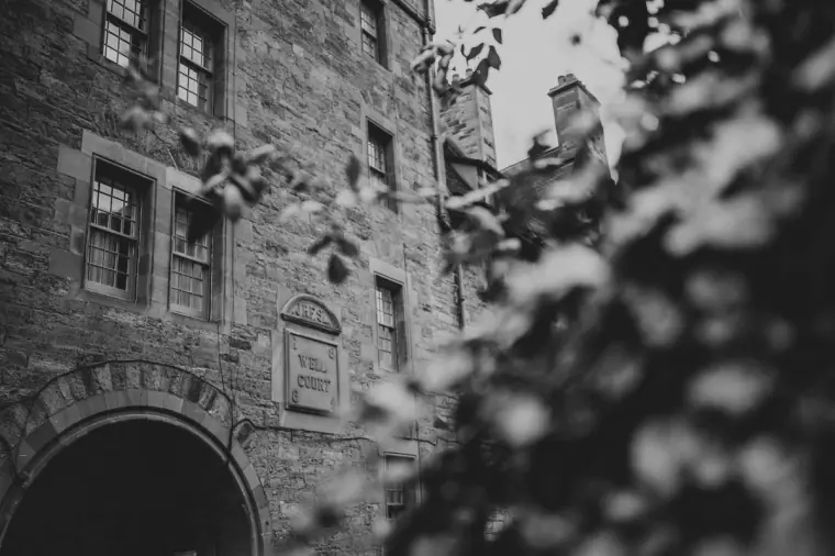 Black-and-white view of a stone tenement and arched doorway framed by leaves