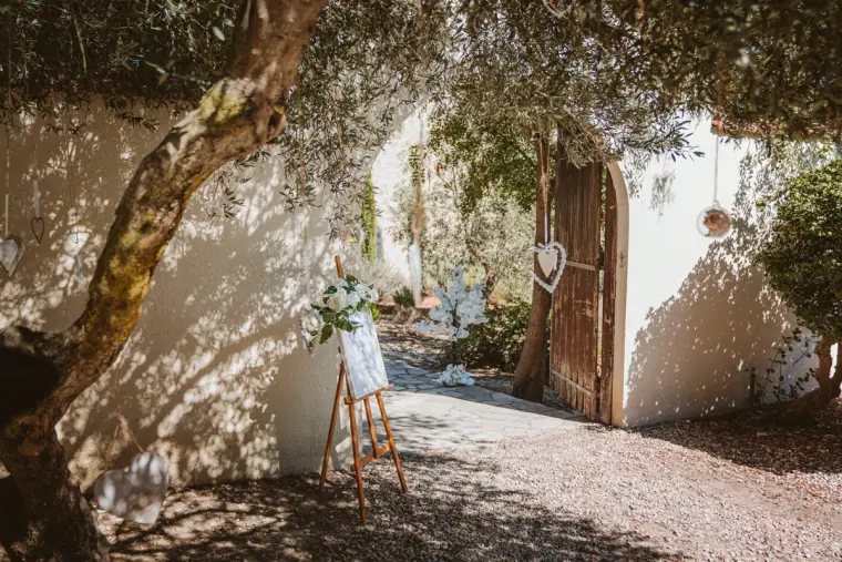Welcome sign on an easel beside an old door shaded by an olive tree