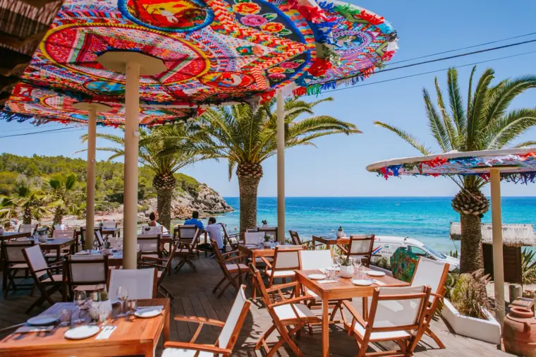 Colourful embroidered parasols shading a seaside restaurant terrace among palm trees, Ibiza