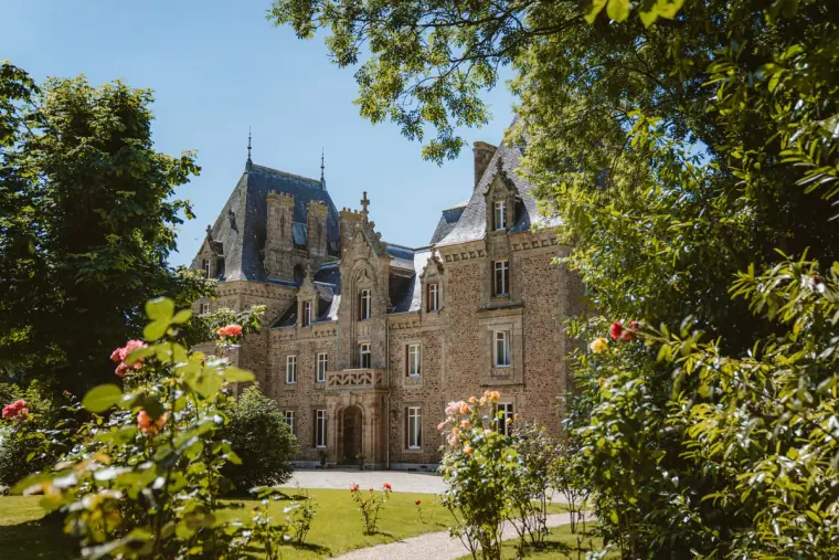 Château de la Basmaignée turrets seen through roses and trees on a sunny day