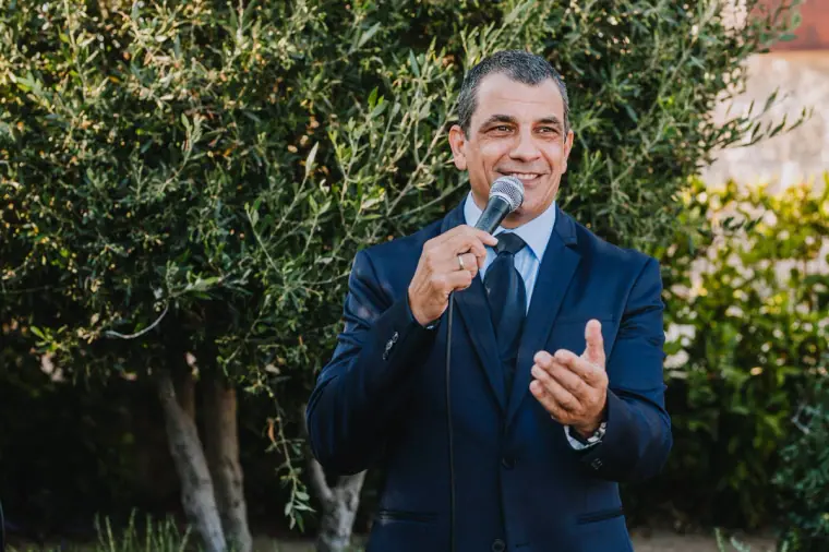 Guest laughing during his microphone speech under olive trees at Liopetro, Kouklia