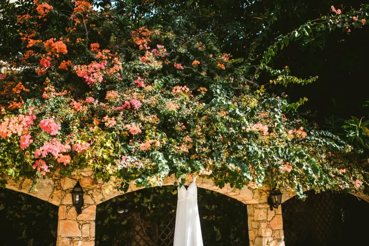 Wedding dress hanging beneath an arch covered in pink bougainvillea