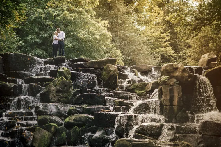 Couple standing on mossy rocks above a cascading waterfall in woodland
