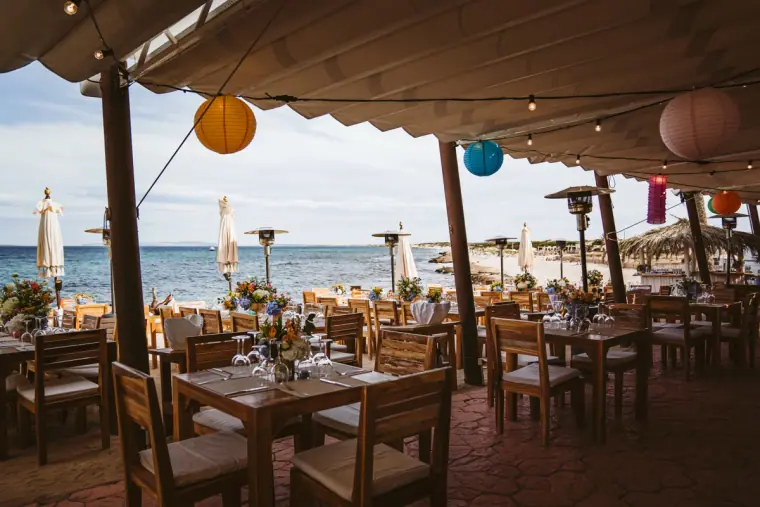 Wooden tables under string lights and colourful paper lanterns on the terrace at La Escollera, Ibiza
