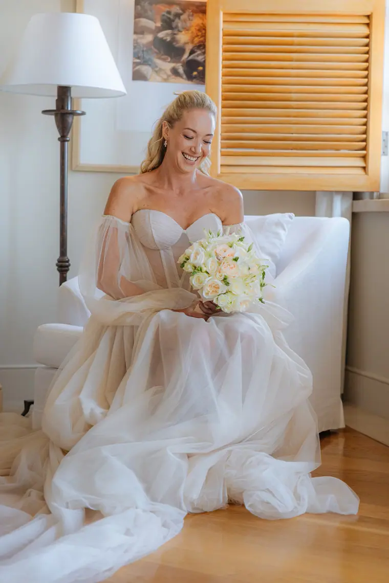 Jade smiling in her armchair with her bouquet beside louvred shutters