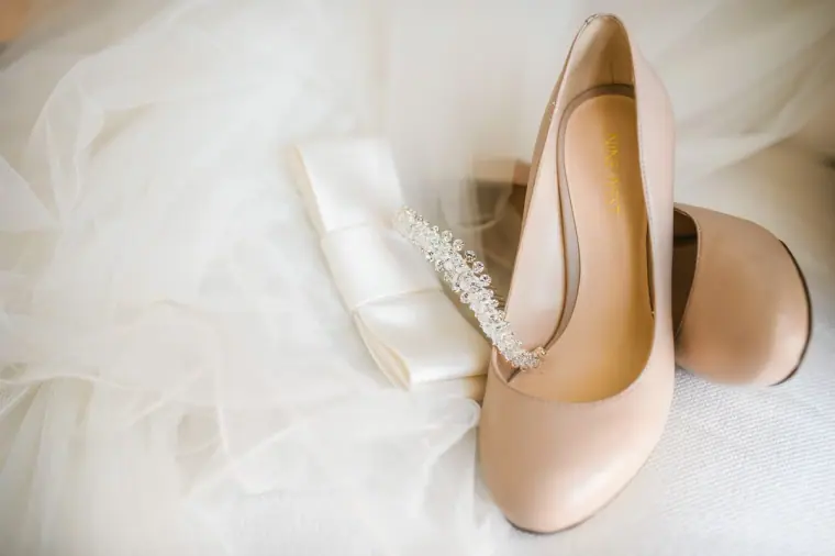 Nude block-heel bridal shoes and a satin clutch resting on tulle