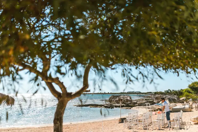 Ceremony chairs being arranged on the beach beneath a pine tree, Thalassines Beach Villas