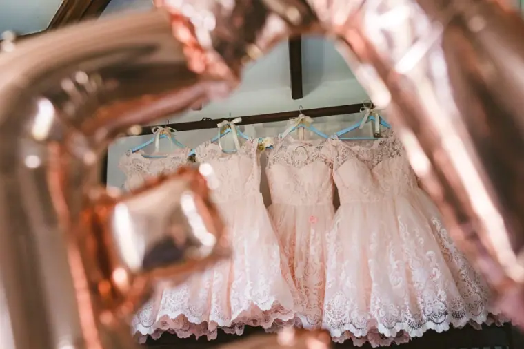 Blush lace bridesmaid dresses hanging in a row, seen through a rose-gold letter