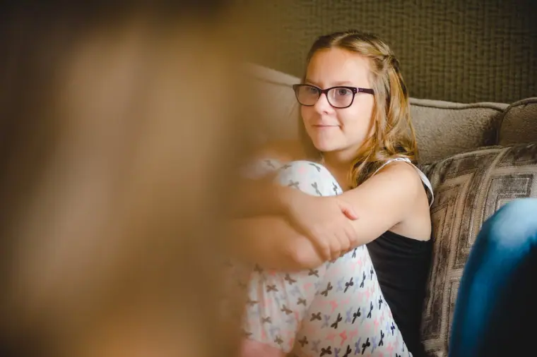 Young bridesmaid in glasses sitting on the sofa during preparations