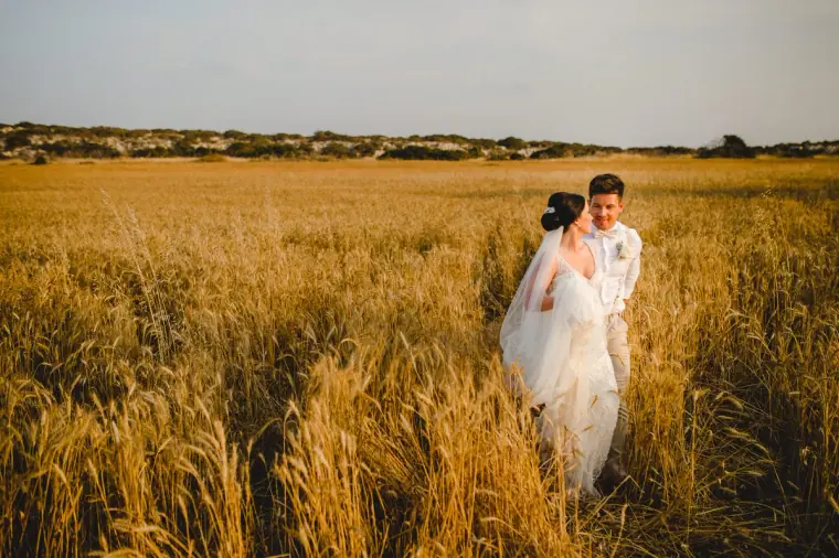 Ellie and James walking hand in hand through a golden wheat field near Ayia Napa