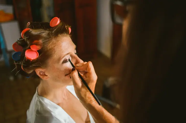 Bride in hair rollers having her eyeliner applied