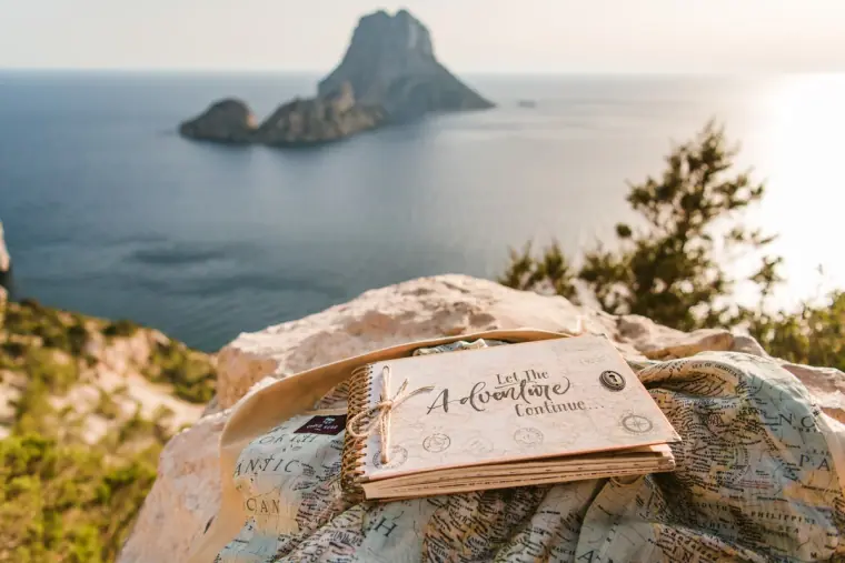 Let the Adventure Continue guestbook resting on a rock with Es Vedrà behind, Ibiza