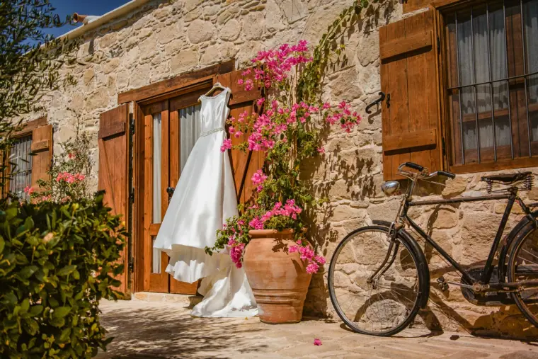 Wedding dress hanging by a stone cottage beside bougainvillea and an old bicycle at Liopetro