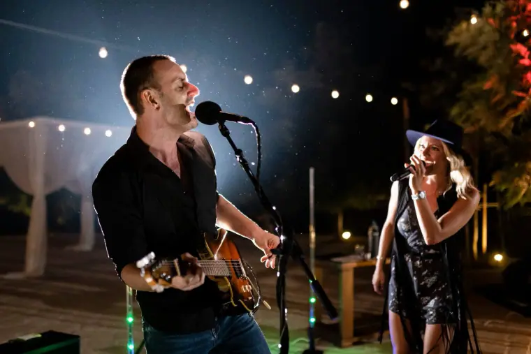 Male guitarist singing alongside Aimie Wild under string lights at an evening wedding