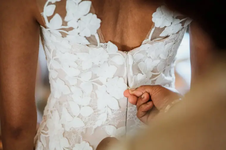Close-up of buttons being fastened on the back of a floral lace wedding dress