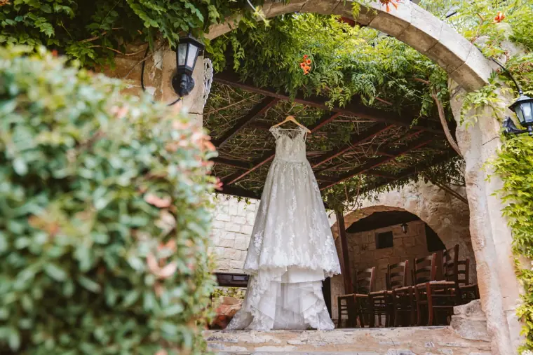 Lace wedding dress hanging beneath the vine-covered stone arch at Vasilias Nikoklis Inn