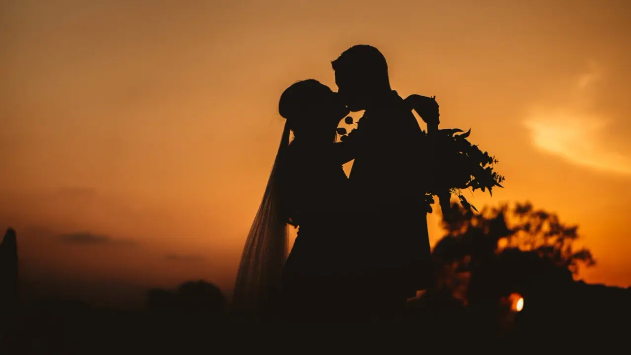 Jemma and Andrew silhouetted in a kiss against an orange sunset at Liopetro, Kouklia
