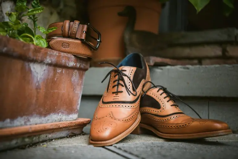 Groom's tan leather brogues and belt on a step beside a terracotta pot