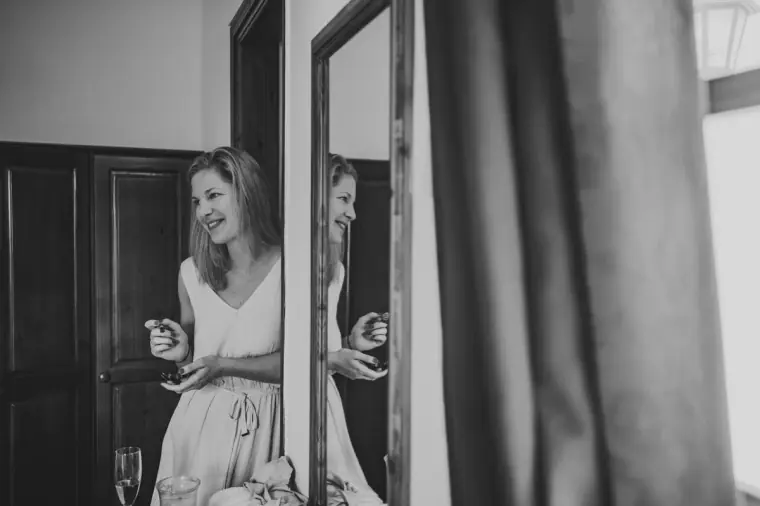 Black-and-white photo of a smiling bridesmaid in a doorway, holding a drink