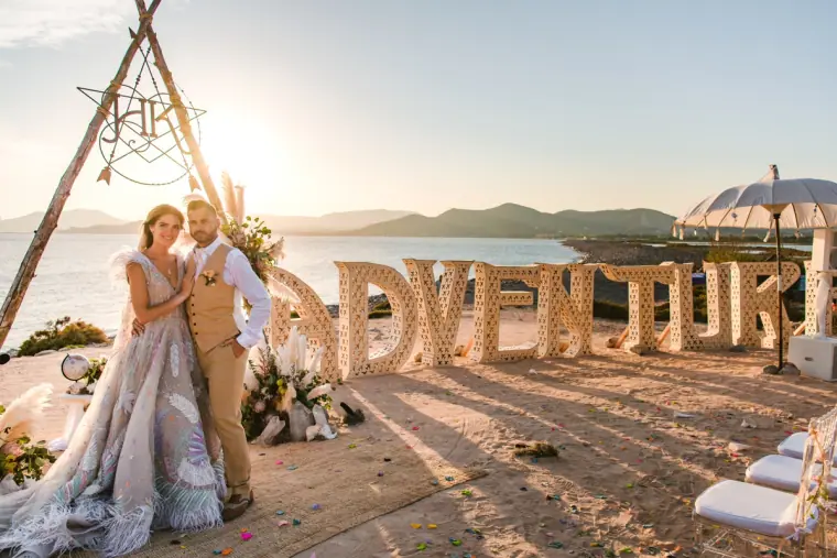 Kenton and Hassiba beside giant ADVENTURE letters at their beach ceremony, Codolar, Salinas