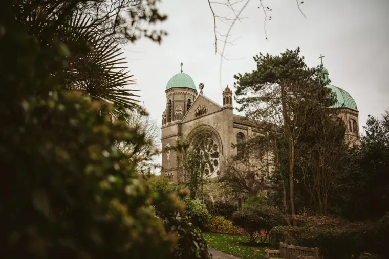 Church with green domes rising behind trees and shrubs in London
