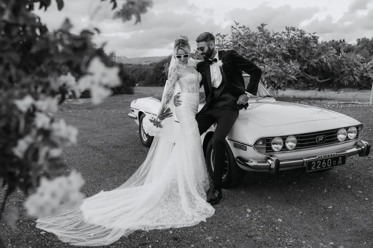 Black-and-white portrait of a couple beside the Triumph Stag in a Cyprus orchard